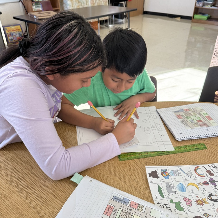 Two students working at a table.  There is a drawing, a ruler, and papers on the table.