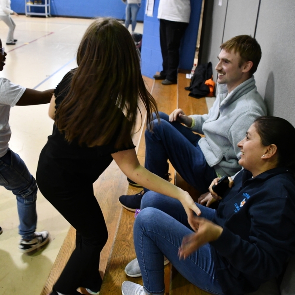 Three girl students invite two staff members to join the dance party in the school gymnasium.