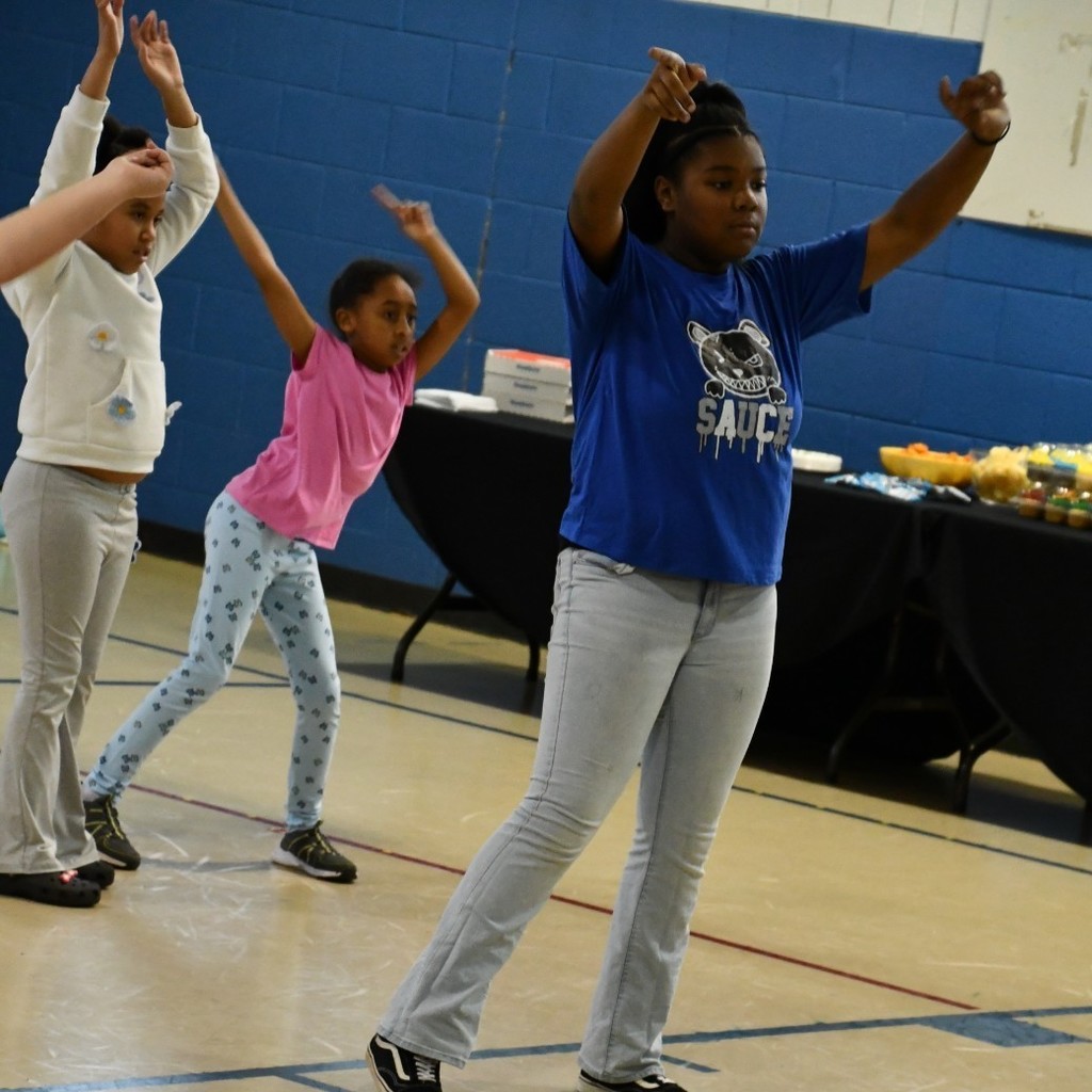 Three students dance in the school gymnasium.