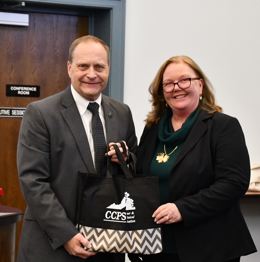 board member holding bag with the CCPS logo standing in board room with superintendent