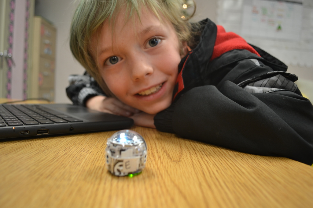 Student smiles for the camera as the ozobot does its programmed code.