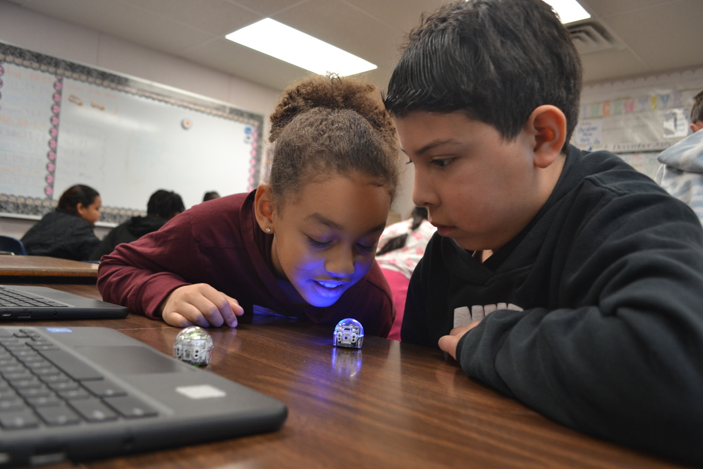 Two students actively watch the coded ozobot move next to the chromebook.