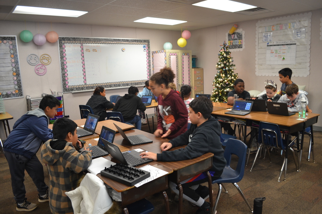 Image shows classroom students working at their desk coding ozobots actively engaged in the lesson.