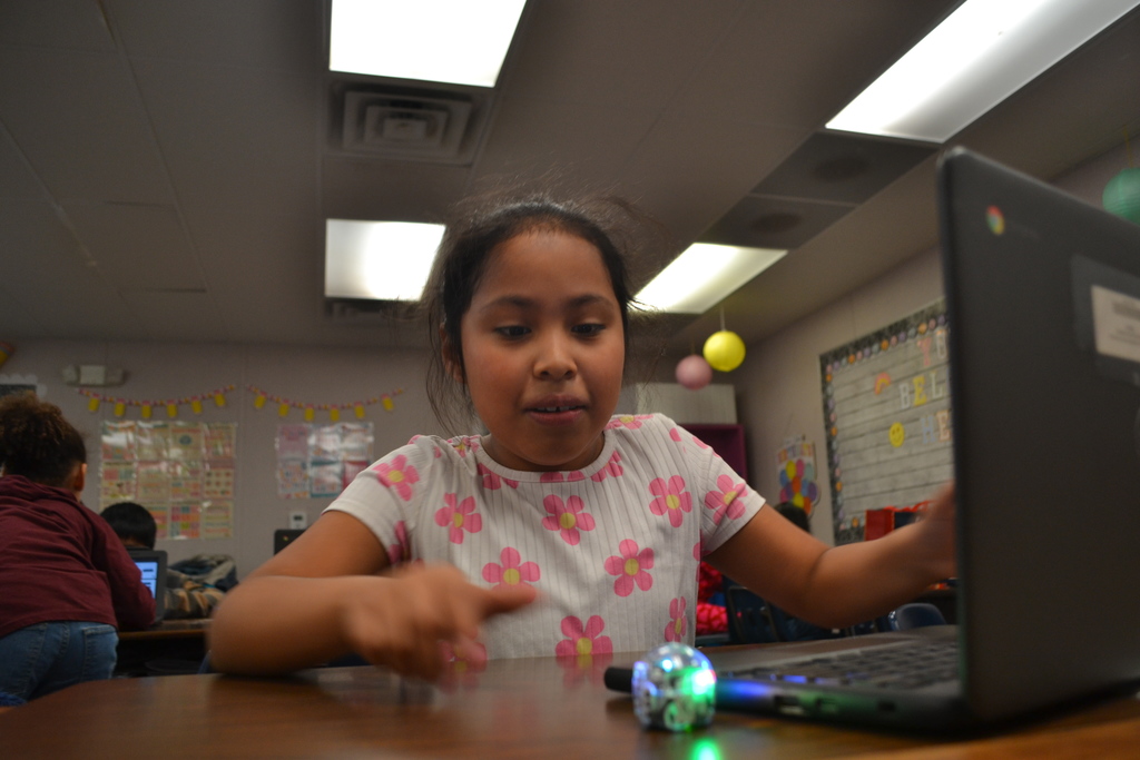 Student actively watches the programmed ozobot move next to the chromebook.