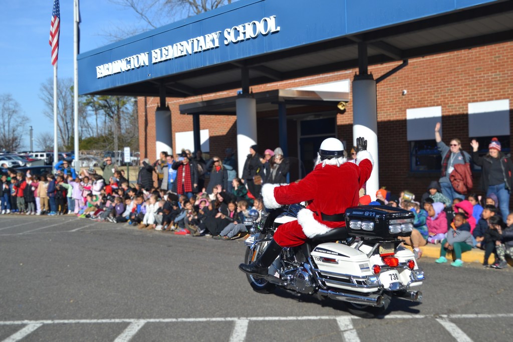 Image contains Santa on a motorcycle waving at students outside in winter coats of Farmington Elementary School