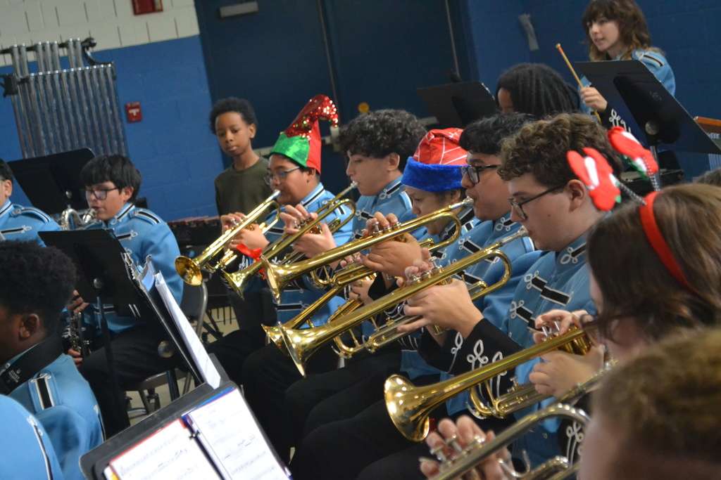 Image contains high school band brass section playing while two elementary students watch them.