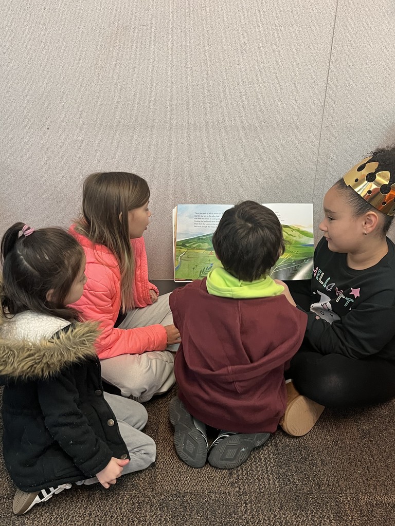 Two  4th grade girls read with 2 preschool students.  Picture shows the backs/sides of their faces.