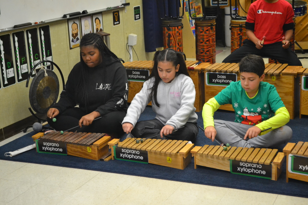 3 students in a row are playing their musical instruments in a music classroom in sync.