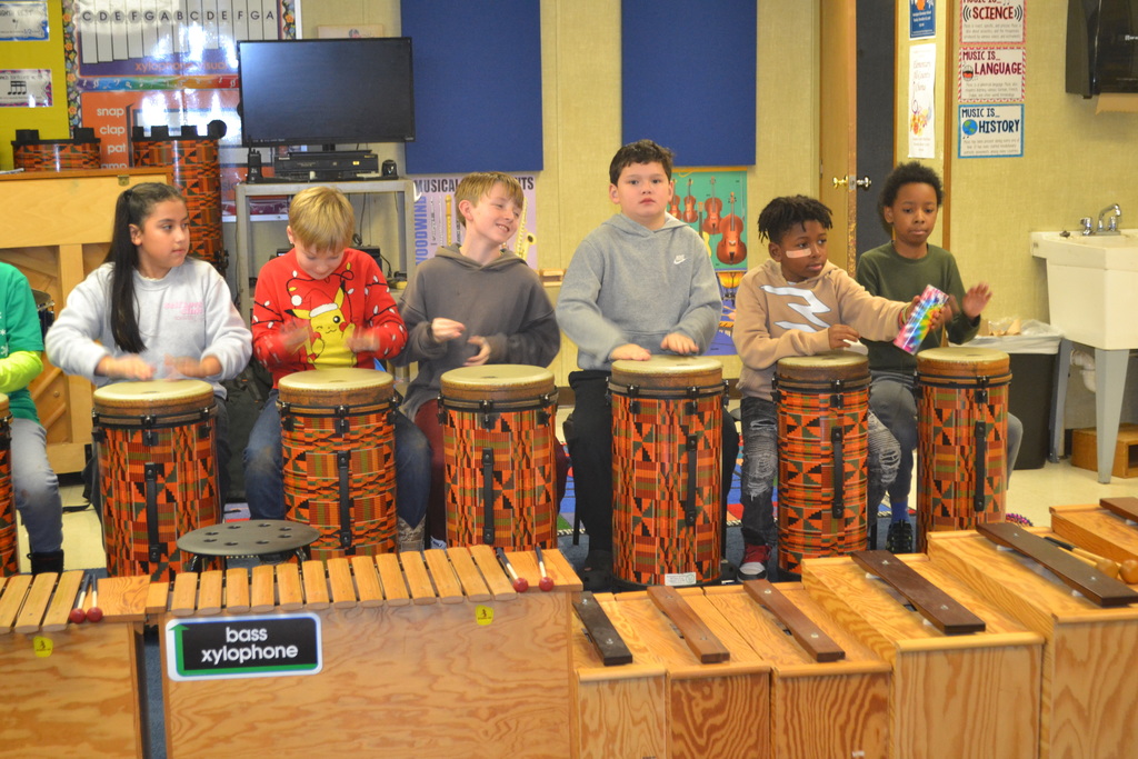 3 students play their ORFF drums in music class together.