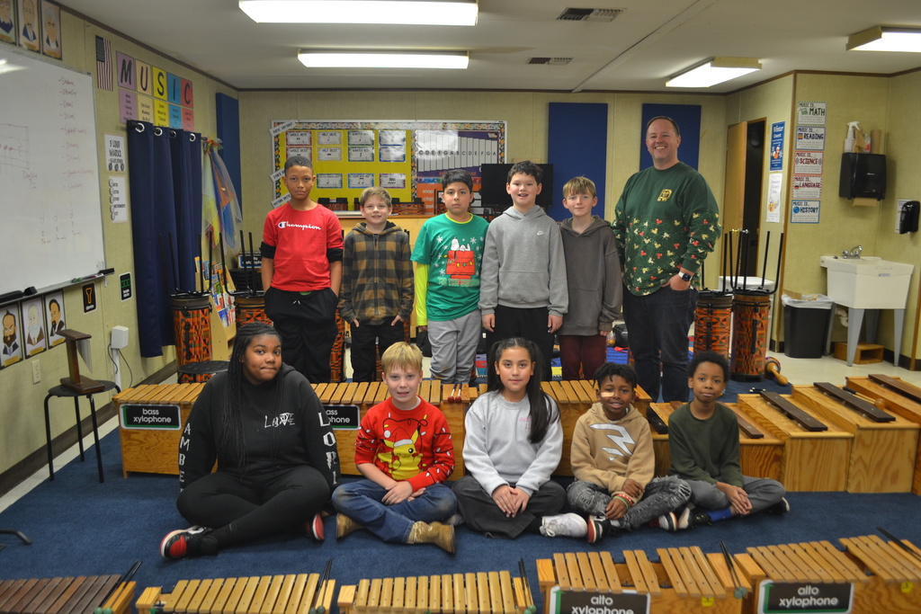 10 students pose for a club picture by their musical instruments in the music classroom with the music teacher.