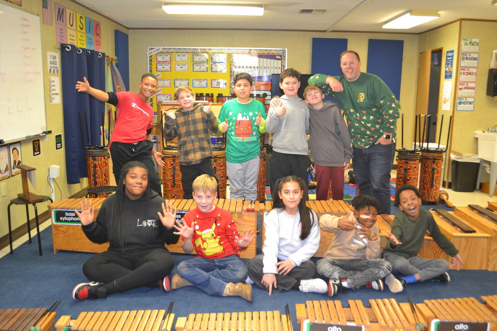 10 student pose joyfully by their music instruments in music classroom with the music teacher.