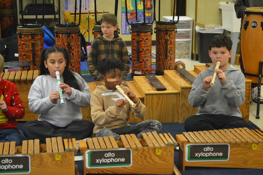 Students are pictured playing their recorders behind other instruments in music class.