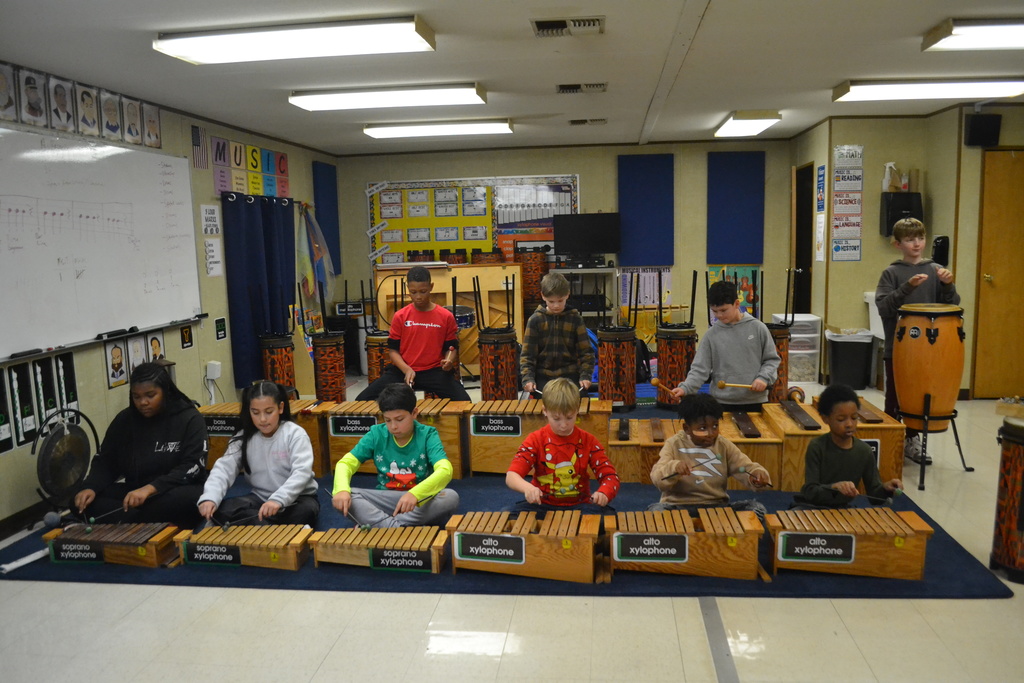 10 students sit behind their instruments in music classroom playing a rehearsed song.