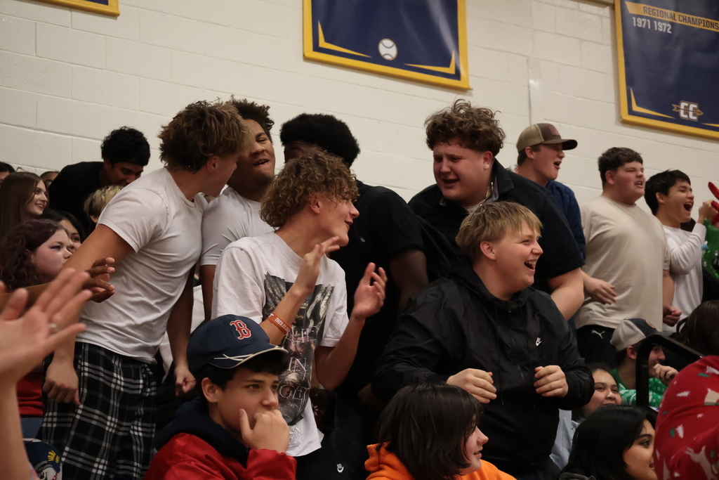Surrounded by a crowd of students, three boys clap and cheer loudly.