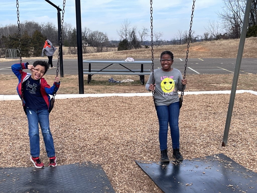 Two students from Mrs. Bopp’s class smile while swinging on the playground during recess on a sunny day.