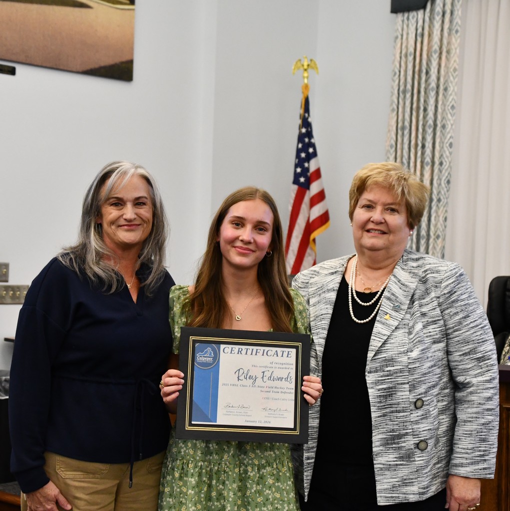 student holding certificate with coach and board member in board room, there is an American flag behind them
