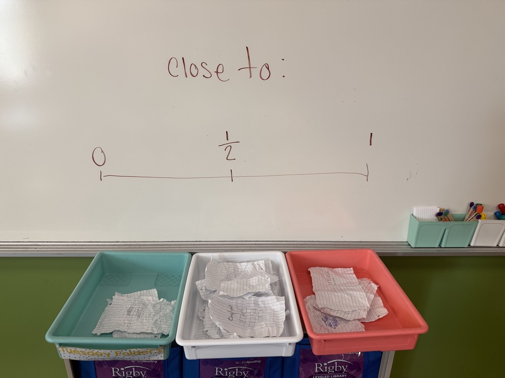 Three colored classroom bins sit beneath a whiteboard displaying a number line labeled 0, 1/2, and 1, with student paper responses placed inside each bin for sorting.