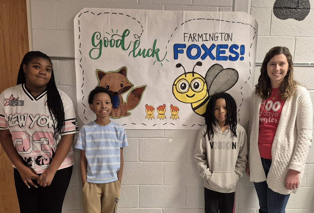 Three students and an adult pose in a hallway in front of a handmade “Good Luck Farmington Foxes!” poster with a fox and bee illustration.