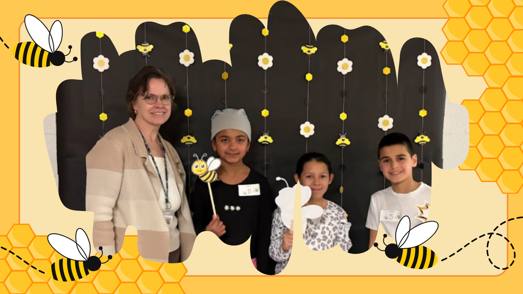 A teacher stands with three elementary students in front of a black and yellow spelling bee–themed backdrop decorated with hanging bees and flowers. The students are holding bee and honeycomb photo props and smiling for the camera. The image is framed with a yellow honeycomb border and cartoon bees flying around the edges.