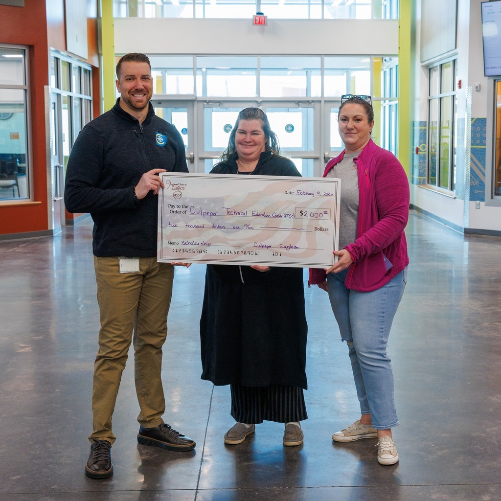 Three adults stand in a school hallway holding an oversized ceremonial check made out to Culpeper Technical Education Center for a $2,000 scholarship donation.