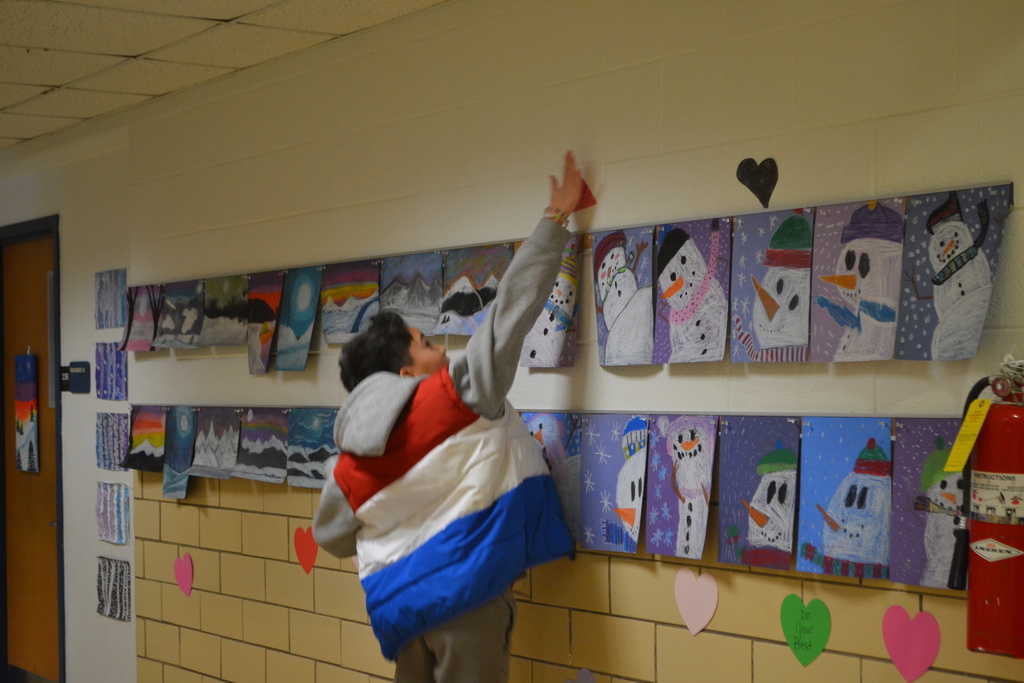 A student jumps to add a paper heart to the wall in the school by snowman artwork.