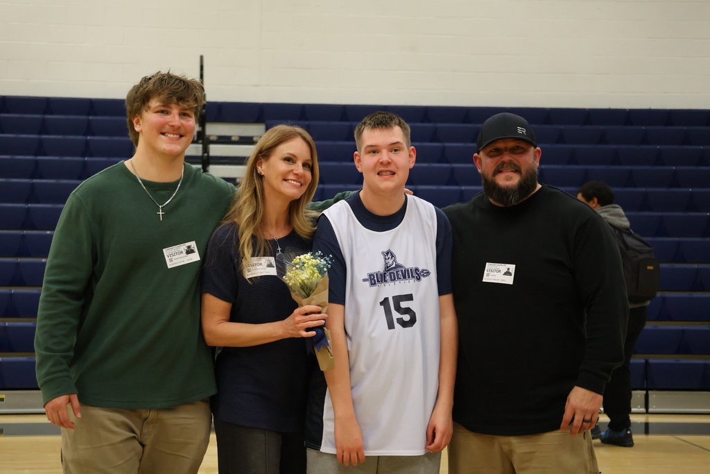 A basketball player smiles with his family for a photo after his senior night game.