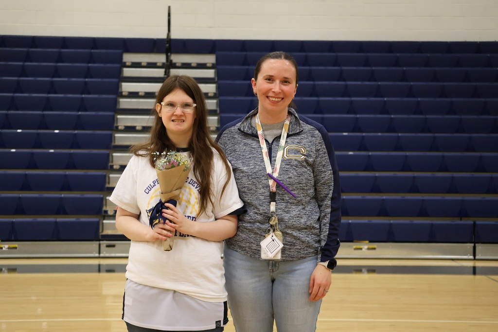 A student holds flowers and poses with her teacher after her basketball senior night.