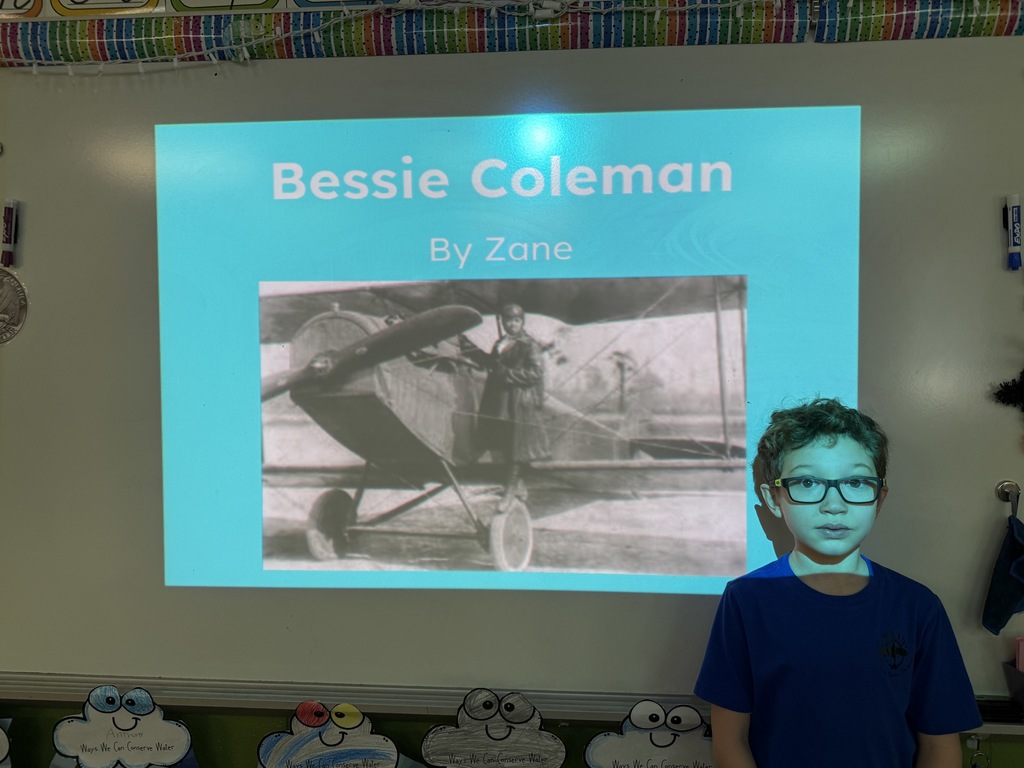 A student stands in front of a projected slide titled “Bessie Coleman” with a black-and-white photo of Bessie Coleman beside an airplane.