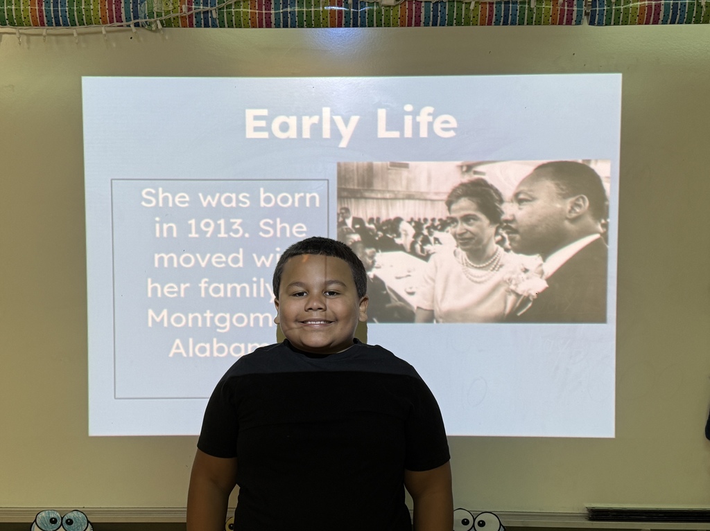 A student stands in front of a slide titled “Early Life” with text about being born in 1913 and moving to Montgomery, Alabama, alongside a historical photo of Rosa Parks and Martin Luther King Jr.