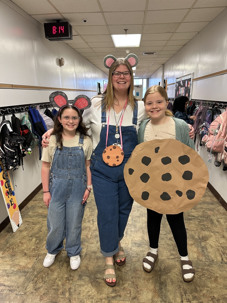 A teacher and two students in a hallway wear mouse ears and a large cookie prop as book character costumes for spirit week.