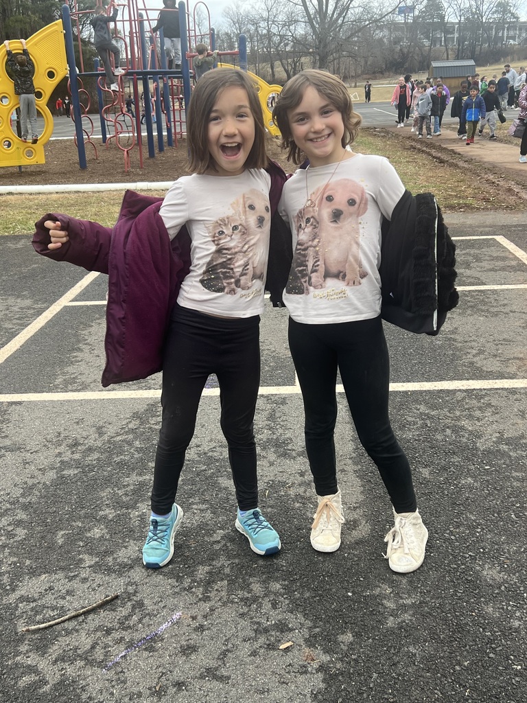 Two students standing outside near the playground smile and pose together wearing matching shirts with pictures of a puppy and kitten for twin day during spirit week.