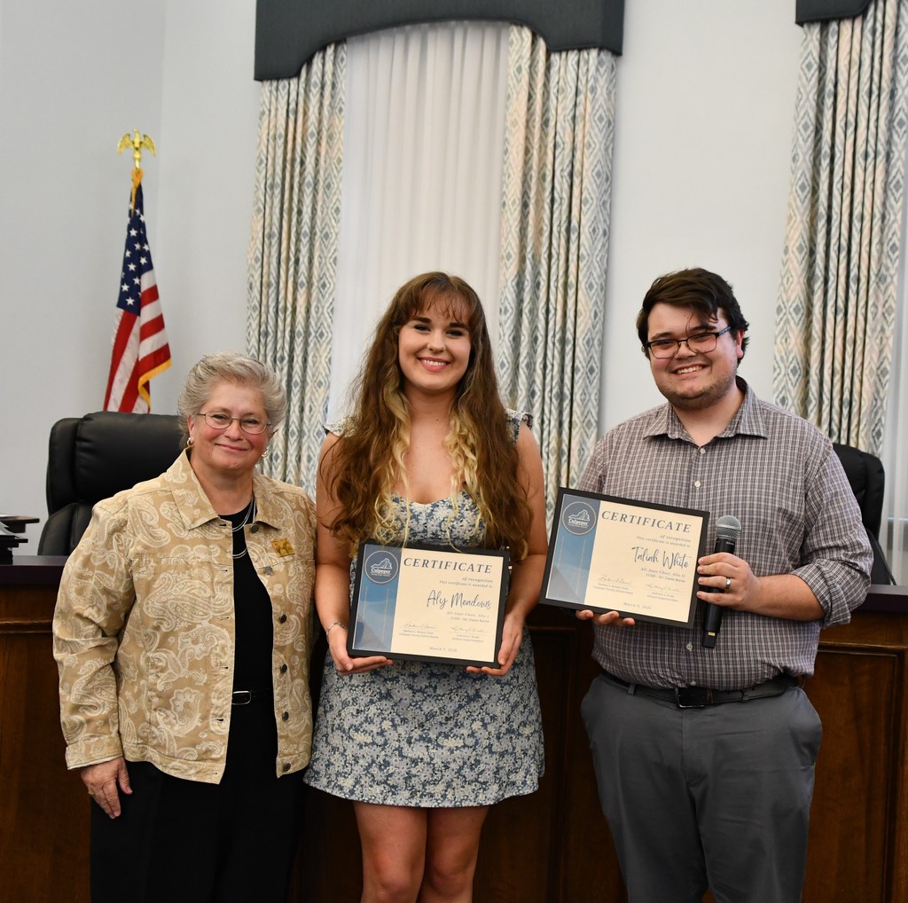 student holding certificate with teacher  and board member in board room