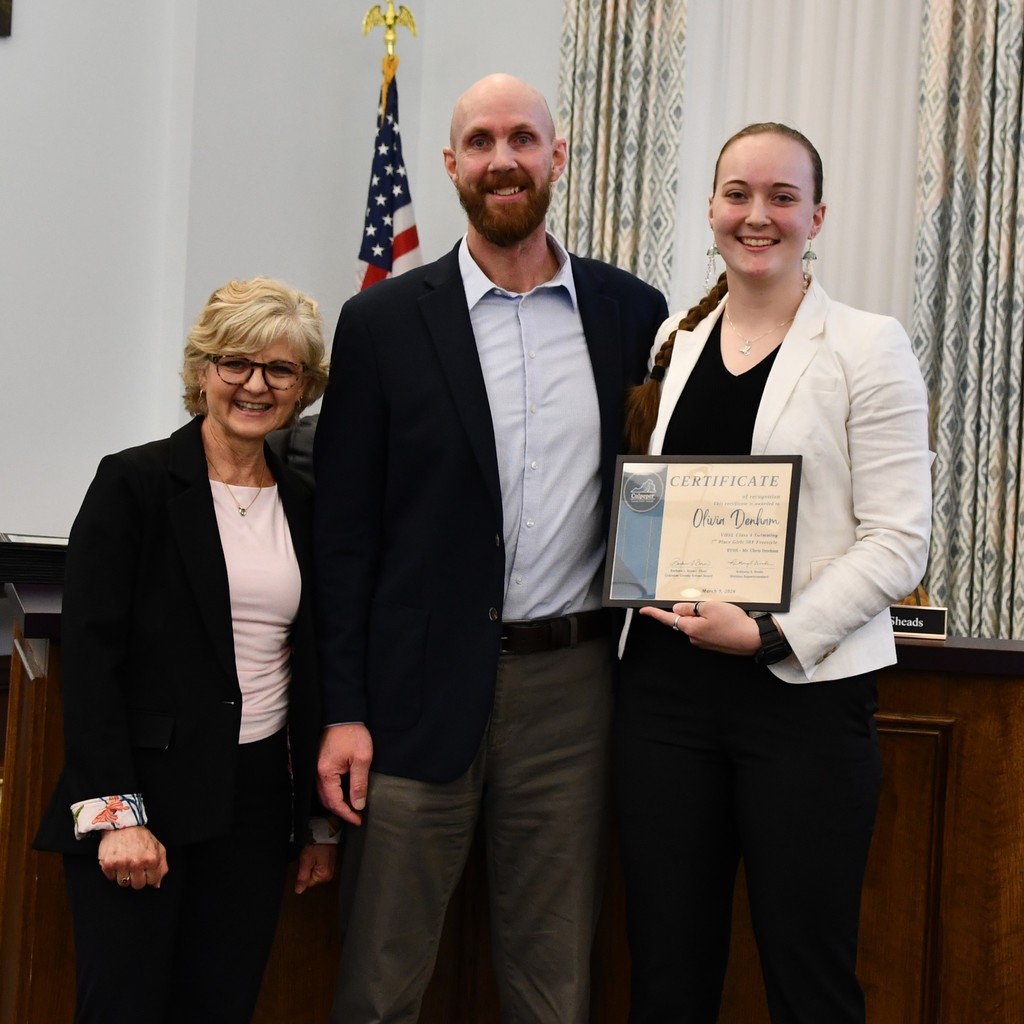 student holding certificate in board room with coach and board member