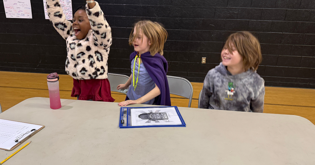 Three students cheer and celebrate at a table during the Battle of the Books competition.