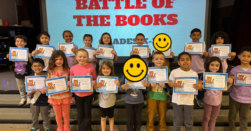 First grade students pose on stage holding certificates for participating in the school’s Battle of the Books reading competition.