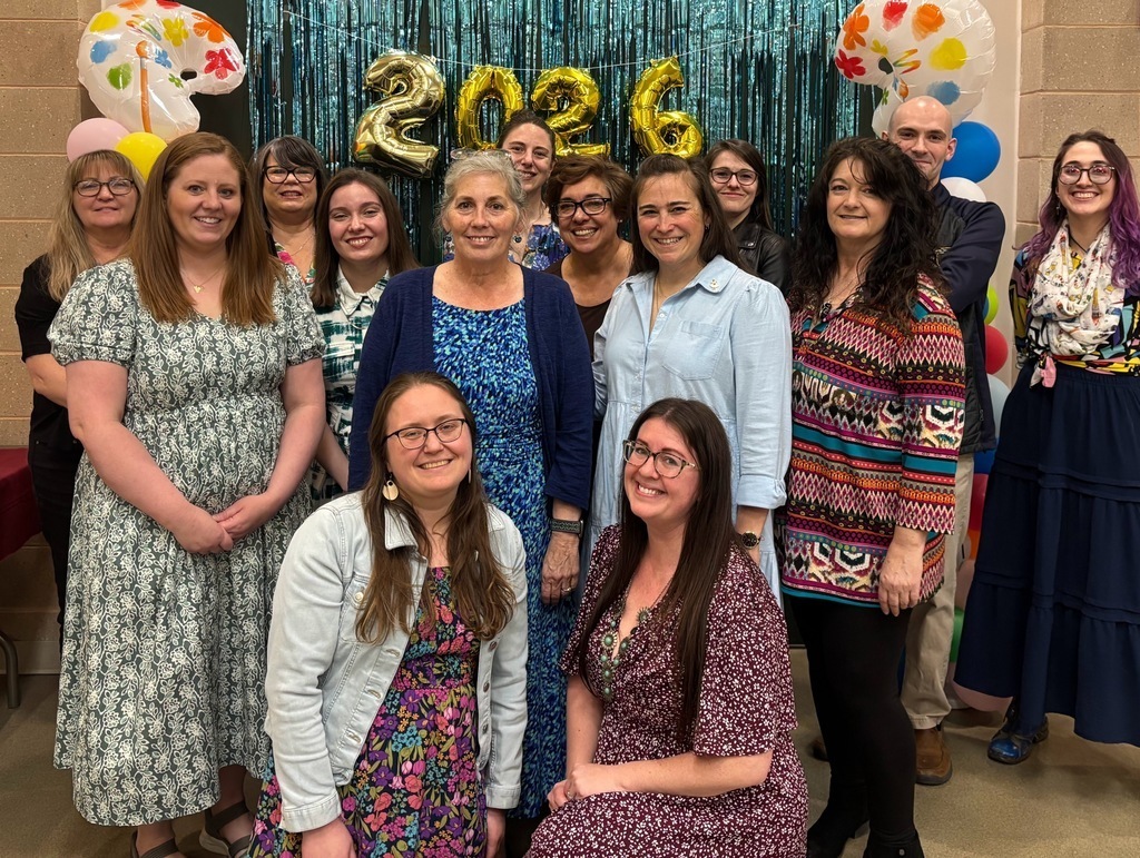 a group of teachers in front of a photo background that has gold balloons across the top that say 2026 and blowup paint palettes on either side