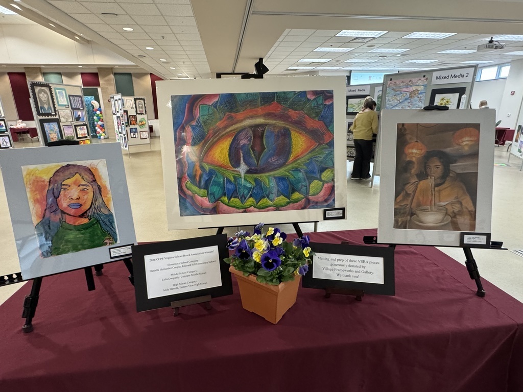 three matted pieces of artwork on display with flowers in a pot on the table in front of them and 2 signs