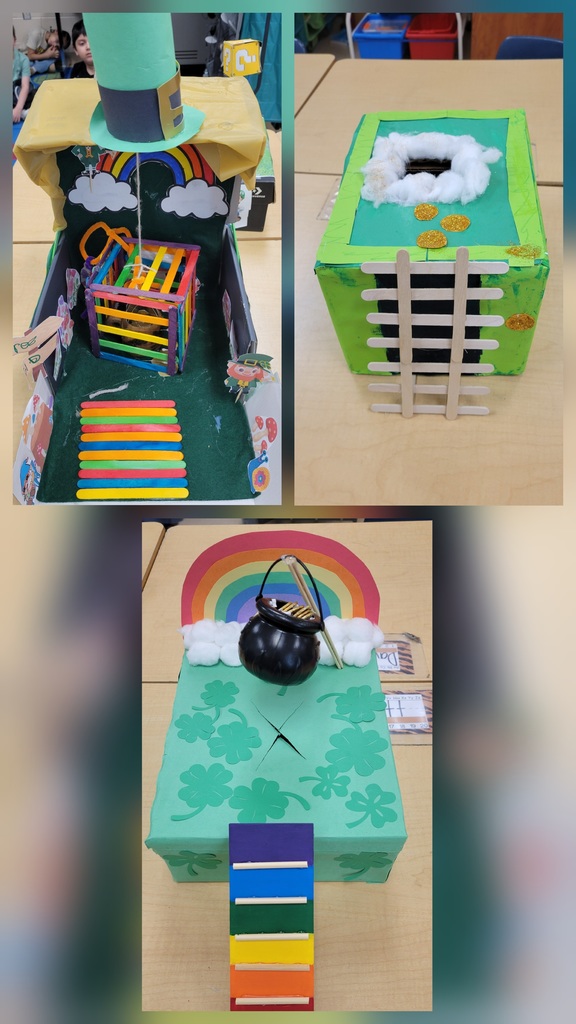 The inside of a decorated box shows a small black pot surrounded by green shredded paper, shamrock cutouts, and rainbow-colored craft sticks.