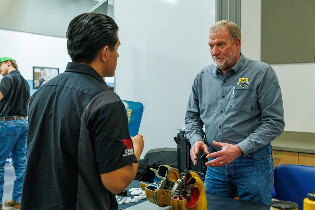 A student speaks with a Carter Machinery representative at a table displaying equipment during a senior job fair.