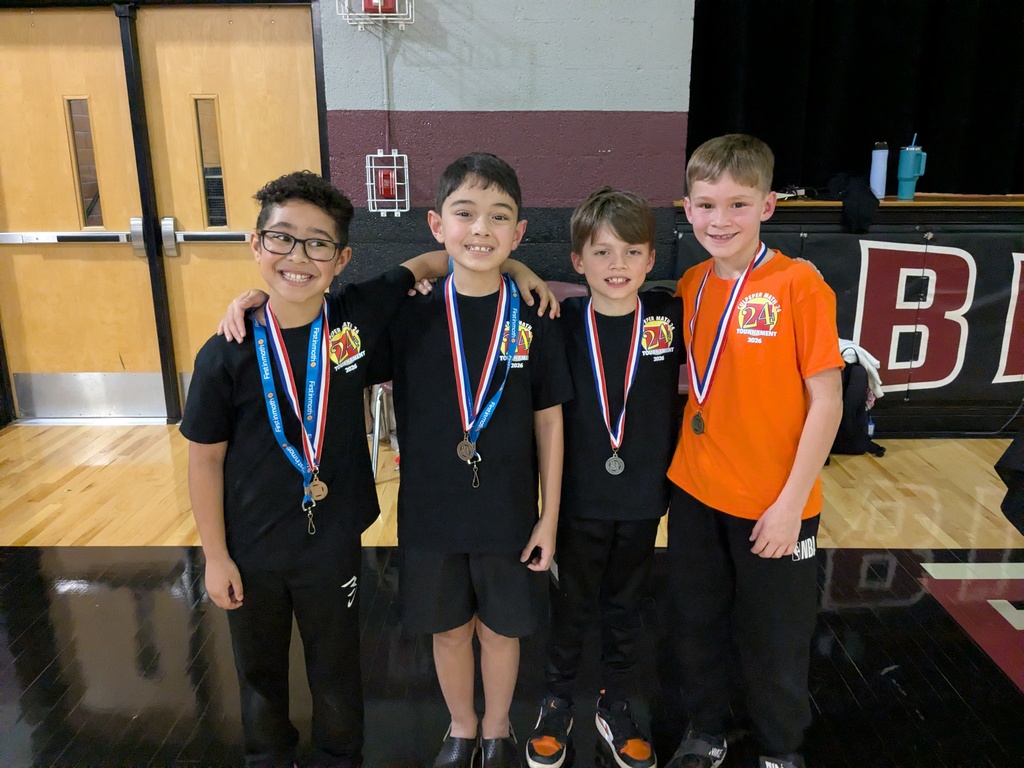 Four elementary students wearing medals stand together with arms around each other, smiling after winning a school competition.
