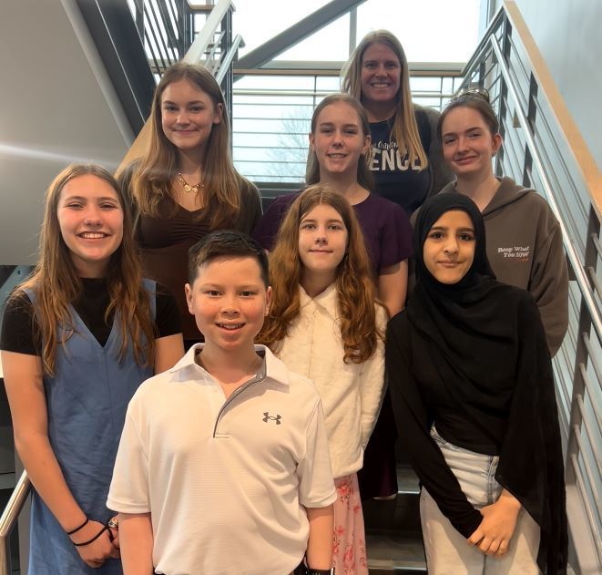 Group of CMS students and a teacher stand together on a staircase, smiling for a group photo at the science fair.