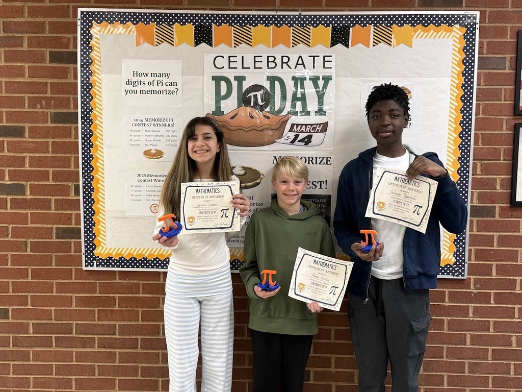 Three middle school students stand in front of a Pi Day bulletin board decorated with orange and black accents and the phrase “Celebrate Pi Day – March 14.” Each student is smiling and holding a certificate of achievement along with a small Pi-themed trophy. The display behind them includes posters about memorizing digits of Pi, highlighting the school’s Pi memorization contest.