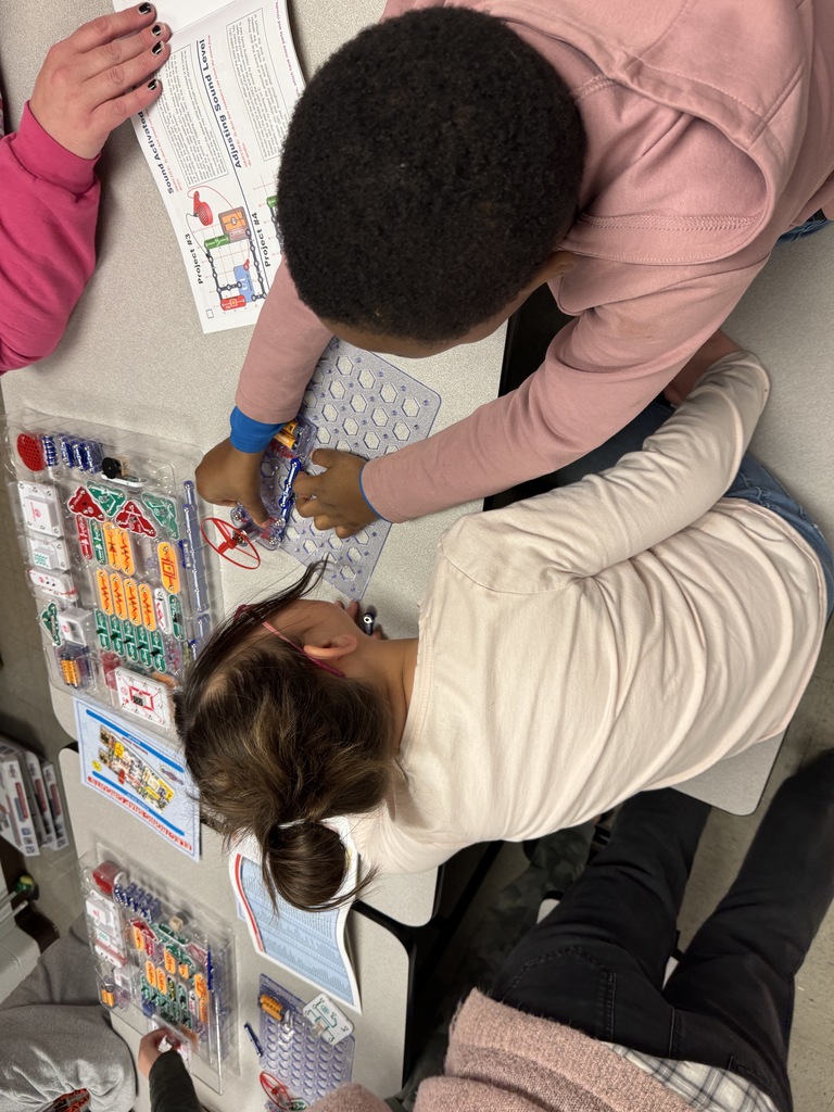 Two students use Snap Circuits kits to build an electrical project while following a printed instruction sheet.