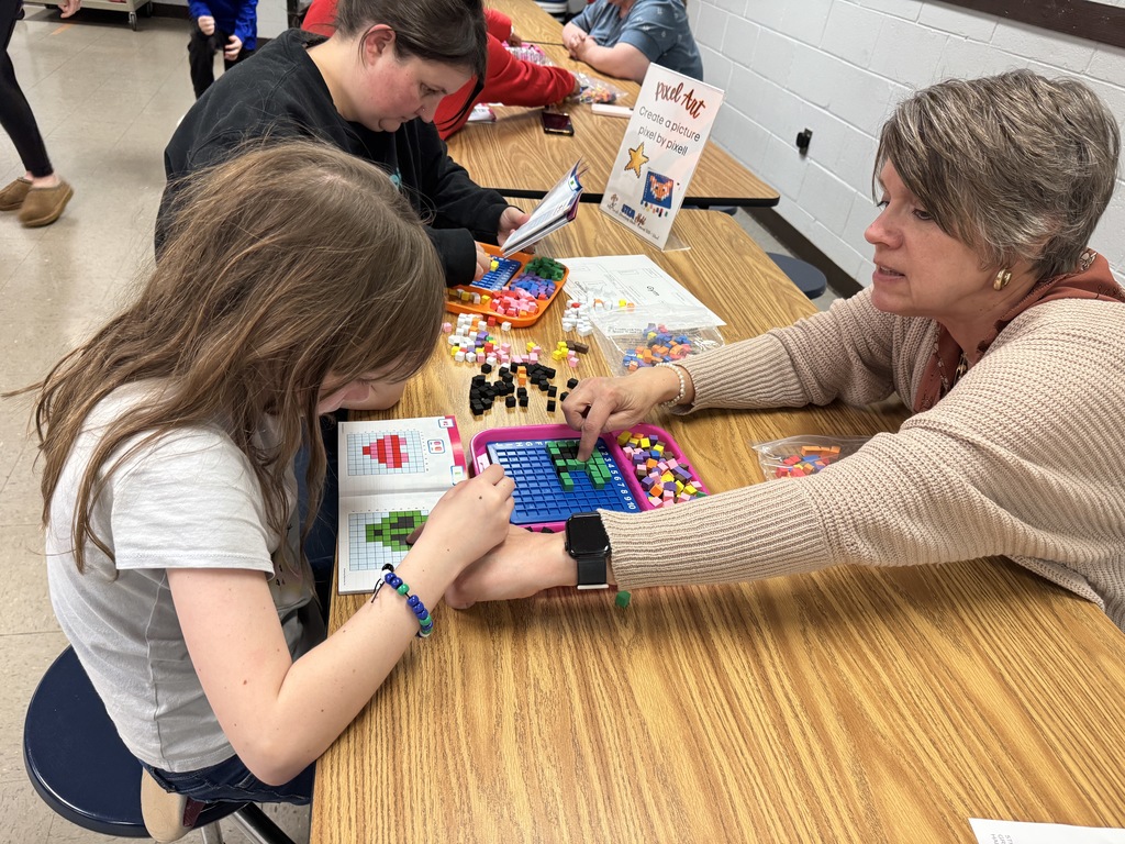A student and adult work together on a pixel art activity using small colored cubes arranged on a grid.