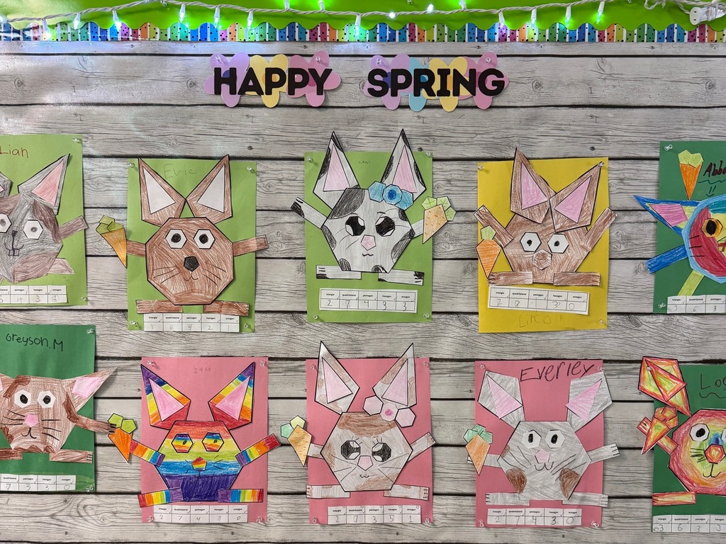 A classroom bulletin board decorated with a “Happy Spring” sign displays student artwork of bunnies made from geometric shapes on colorful paper backgrounds.