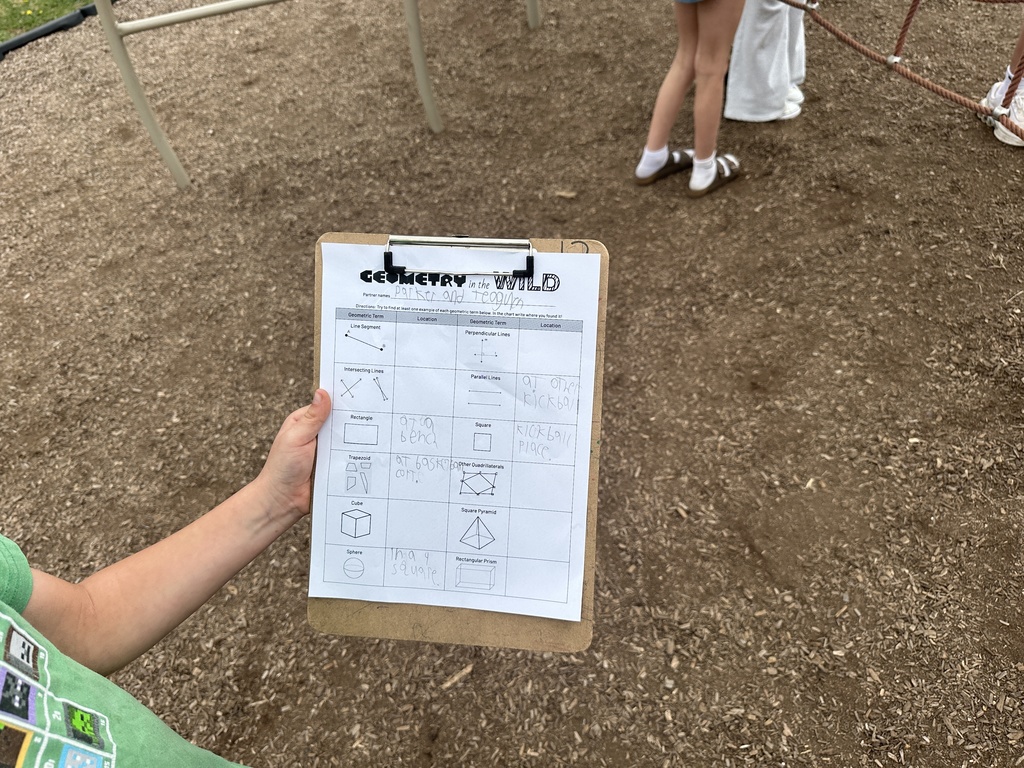 Close-up of a student holding a clipboard with a “Geometry in the Wild” worksheet, identifying shapes like rectangles, squares, and parallel lines found around the playground.