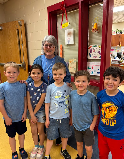 “Teacher and a group of five elementary students pose together in a school hallway, many wearing blue to recognize Autism Awareness Day.”