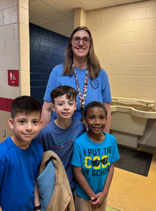 “Teacher and three elementary students stand together in a hallway, smiling and wearing blue to support Autism Awareness Day.”