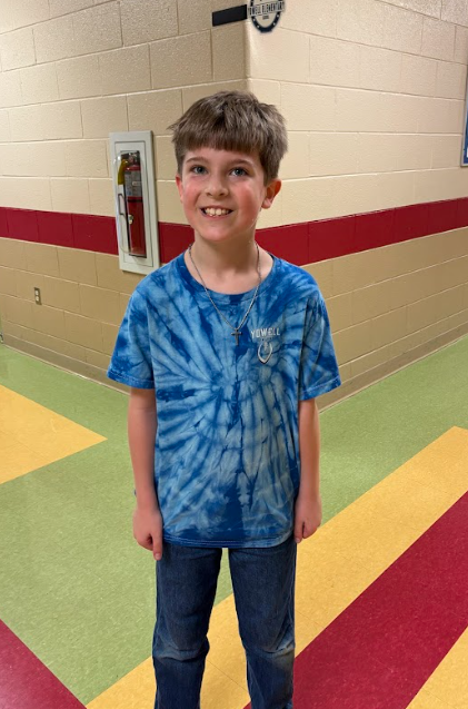 “Elementary student standing in a school hallway wearing a blue tie-dye shirt and smiling for Autism Awareness Day.”