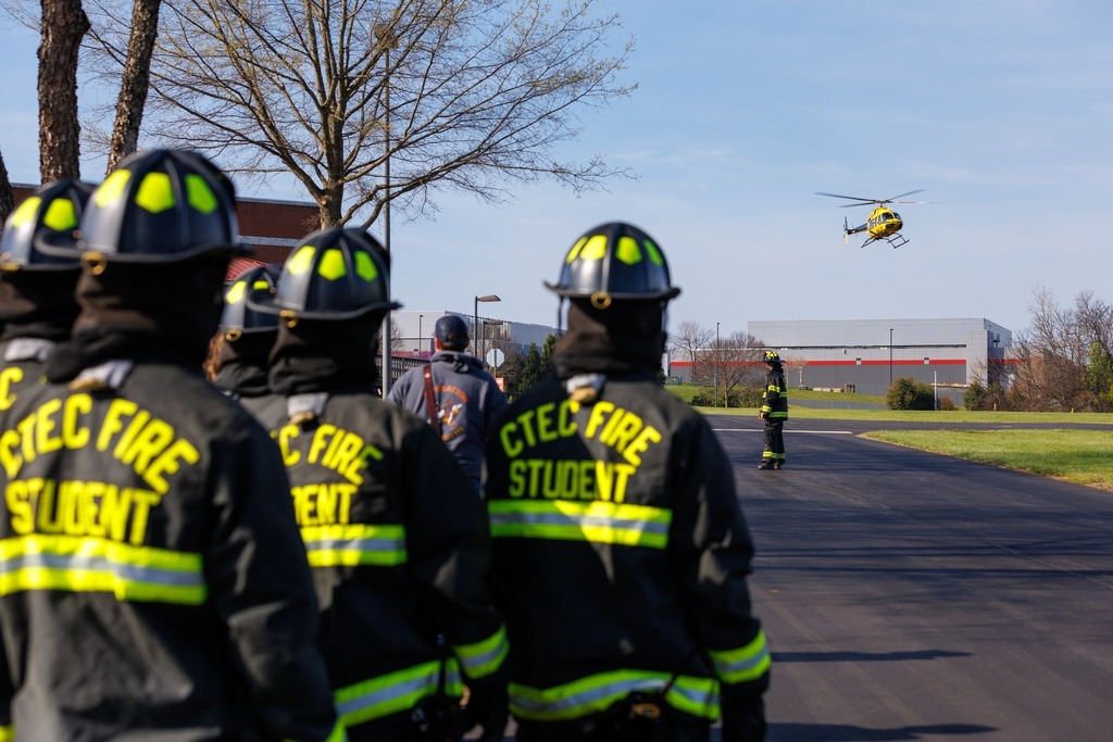 CTEC Fire students in full gear stand in a parking lot watching as the AirCare 6 medical helicopter approaches.